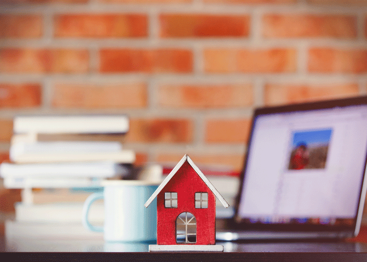 House-shaped trinket on a desk next to a laptop and a stack of books on various appraisal topics