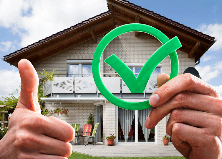 Real estate appraiser hoding a check mark and a thumbs-up symbol up in front of a house