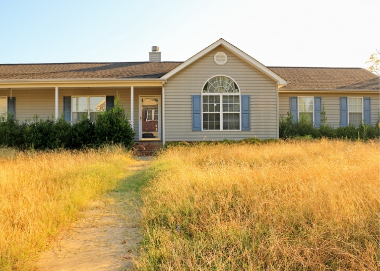 Foreclosed ranch style home with overgrown lawn