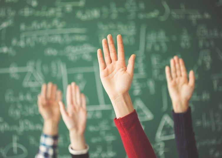 Students' hands raised in front of green chalkboard coverd in math problems
